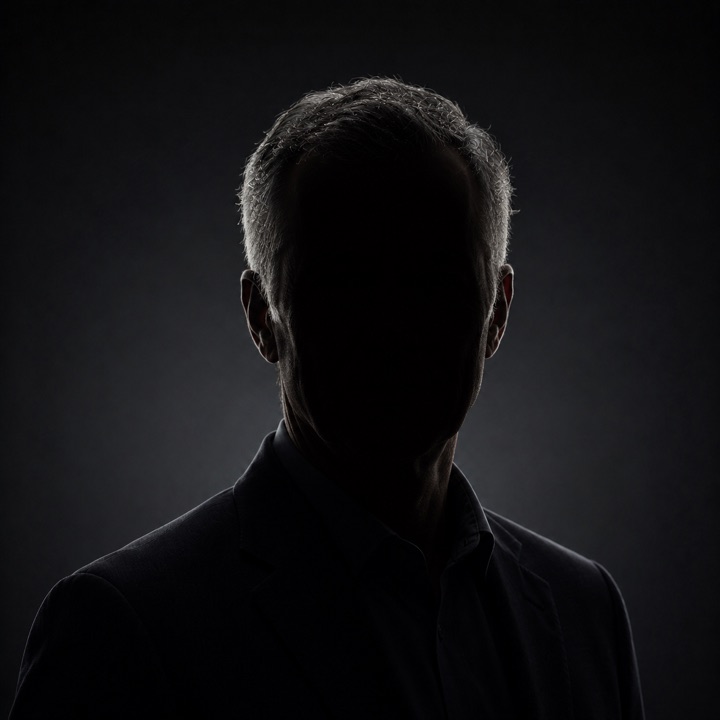 A man photographed in near-darkness, his face lost in shadow
